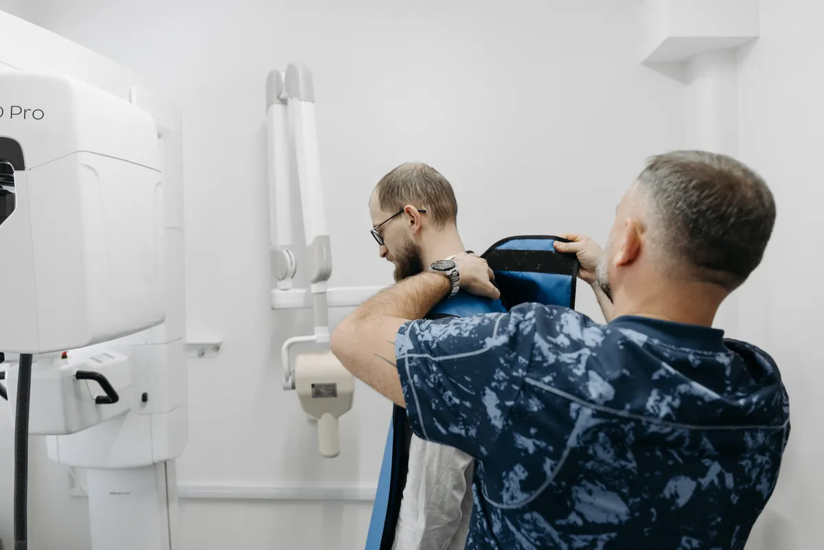 A radiographer positioning a patient carefully at an X-ray unit for a specified view.